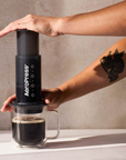 Person using an Aeropress coffee maker on a kitchen counter with a plant in the background.