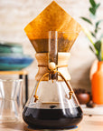 Chemex coffee maker with a paper filter on a wooden surface.
