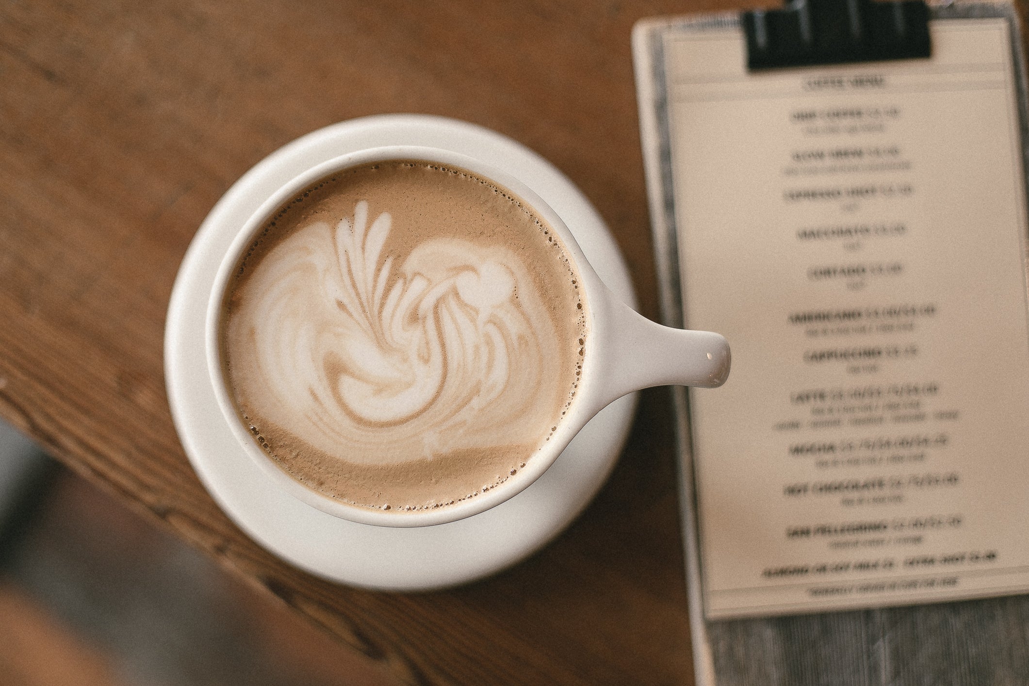 A latte with swirled milk and a out of focus menu on a cafe bar